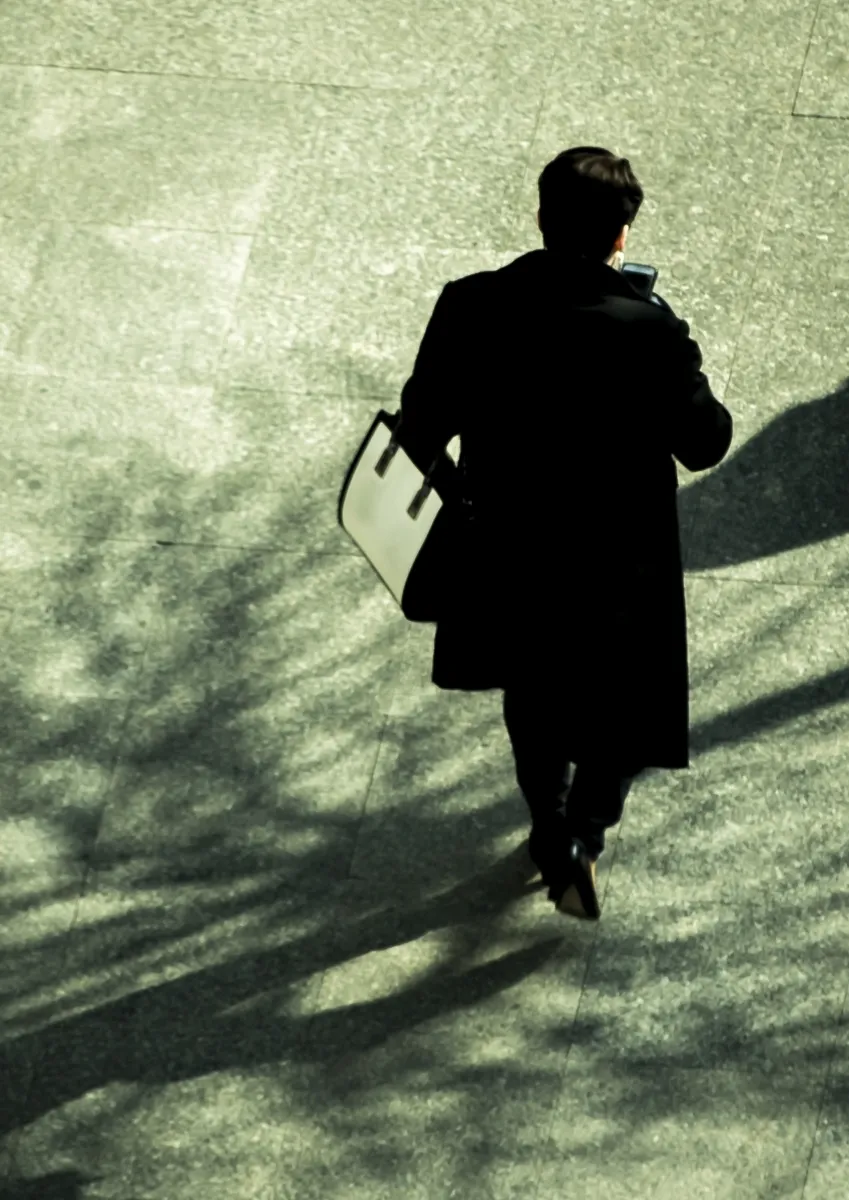 Overhead view of a person in a dark coat walking with a white shoulder bag and a phone
